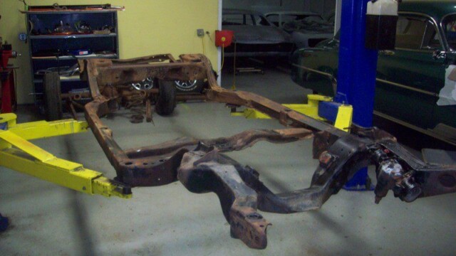 Rusty car chassis on lift in garage.