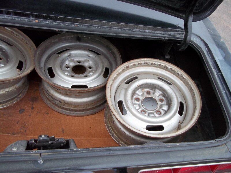 Three rusty vintage car rims in trunk.