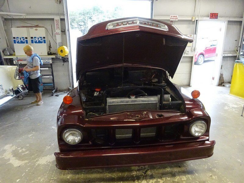 Here's an 8-word alt tag for the image: Burgundy classic car with hood open, engine visible.