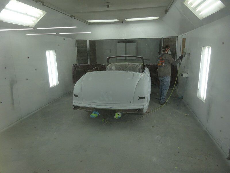Classic car being painted in a booth.