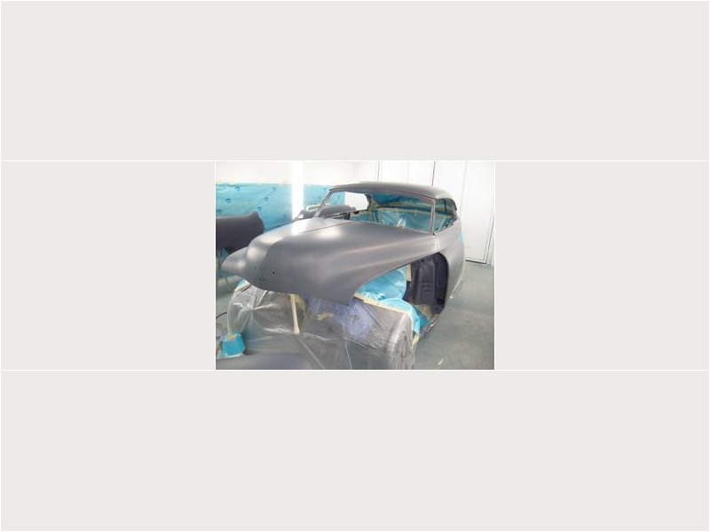 Here's an alt tag for the image: `Gray primered classic car body in shop.`