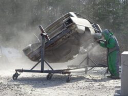 Sandblasting a car body outdoors.