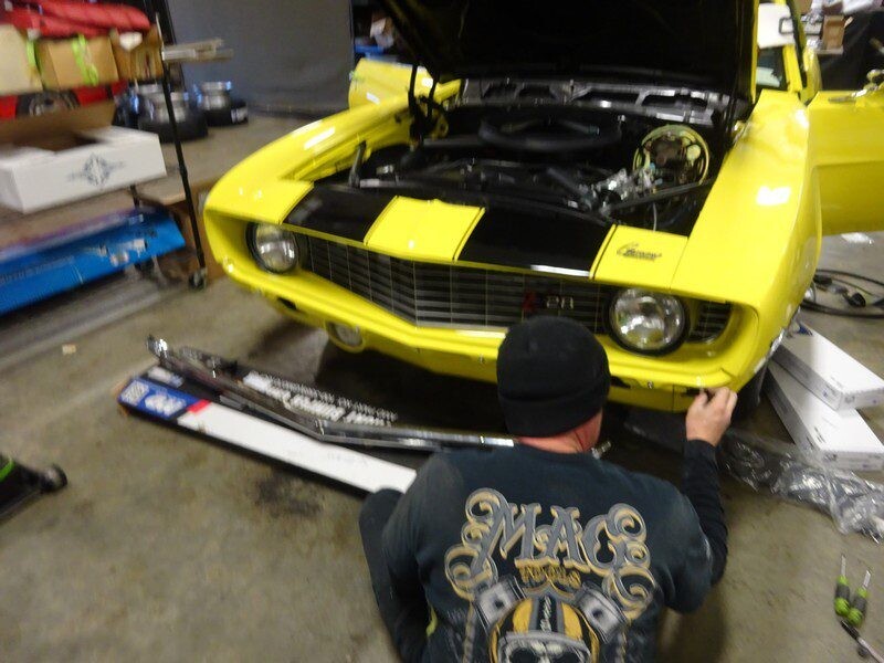 Mechanic installing parts on yellow Camaro.