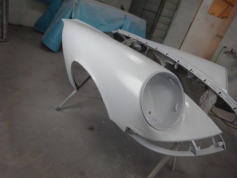 Here's an 8-word alt tag for the image: White car body part, freshly painted, in shop.