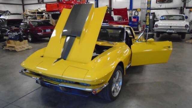 Yellow Corvette with hood up in garage.