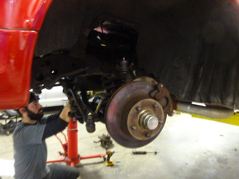 Mechanic repairing a red truck's suspension.