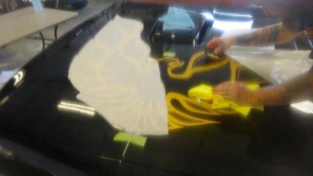 Person applying gold decal to car hood.