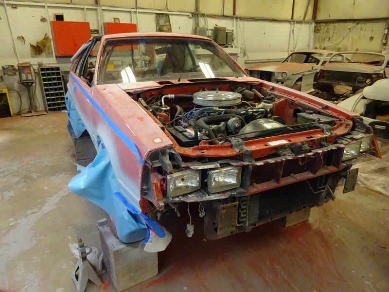 Red car undergoing restoration in shop.