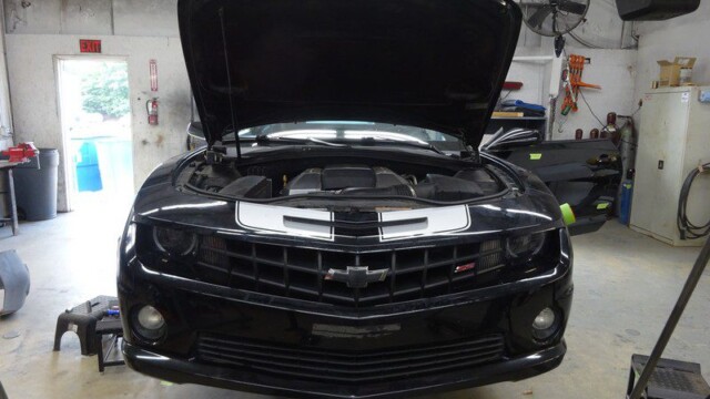 Black Camaro with hood open in garage.