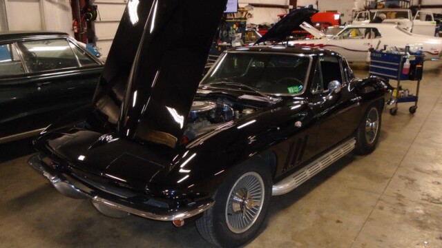 Black Corvette with hood open in garage.