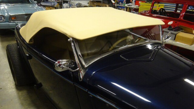 Here's an 8-word alt tag for the image: Cream-top dark blue hot rod roadster in shop.
