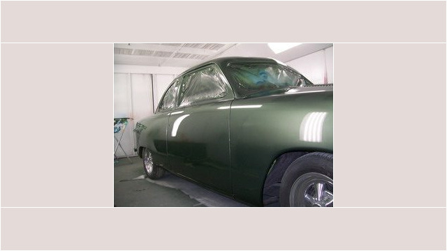 Here's an alt tag for the image: Dark green classic car in paint booth.