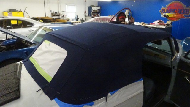 Here's an 8-word alt tag for the image: Dark blue convertible top being installed on classic car.