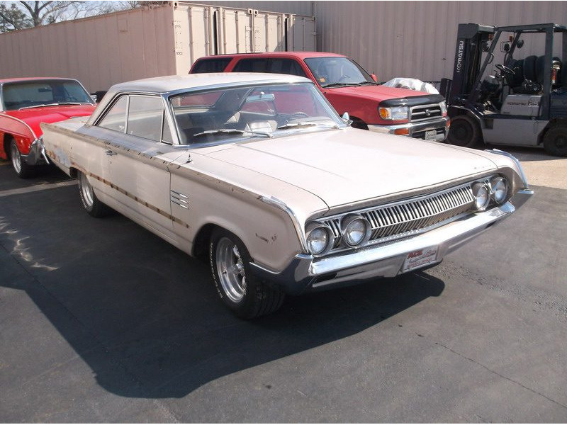 Cream-colored classic car in parking lot.