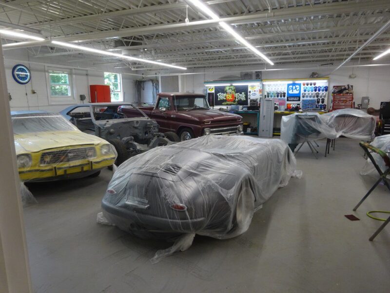 Classic cars under plastic covers in garage.