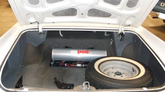 Here's an 8-word alt tag for the image: White car trunk with spare tire and air pod.