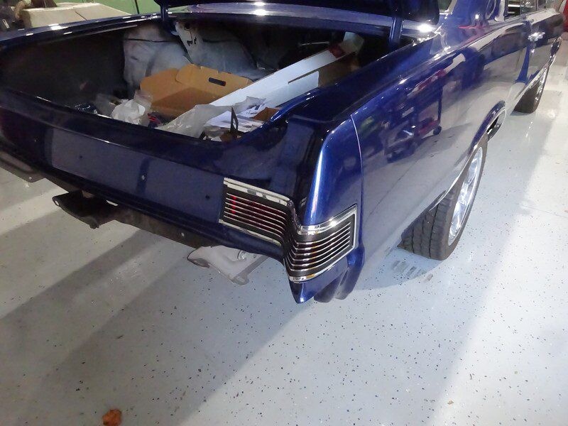 Here's an 8-word alt tag for the image: Blue classic car's rear, trunk open, in garage.