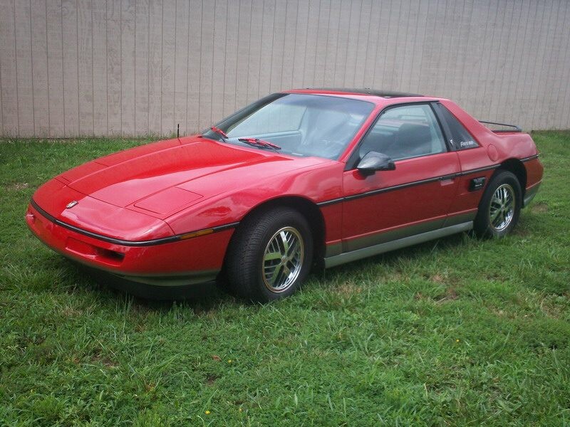 Red Pontiac Fiero parked on grass.