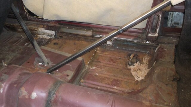 Rusty car floor with metal support bars.