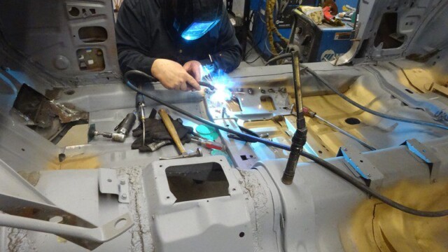 Welder repairing car floor with sparks.