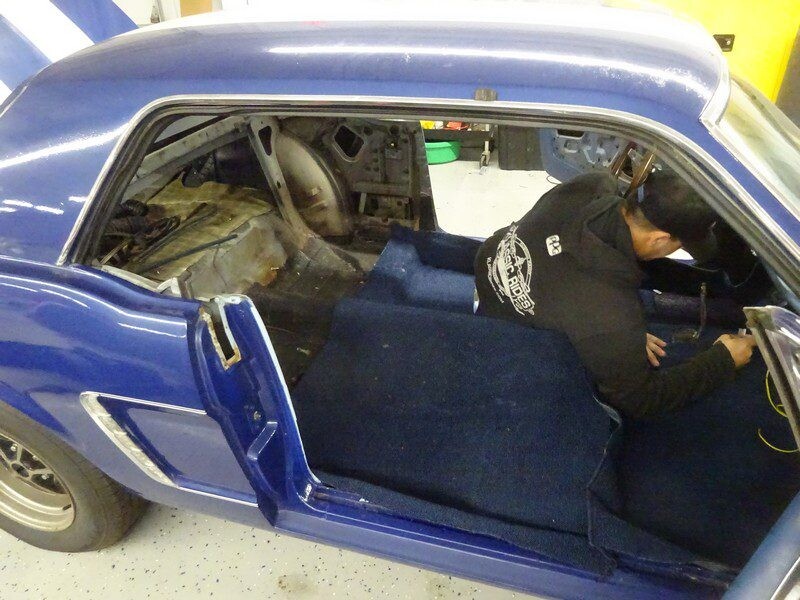 Mechanic installing carpet in blue Mustang.