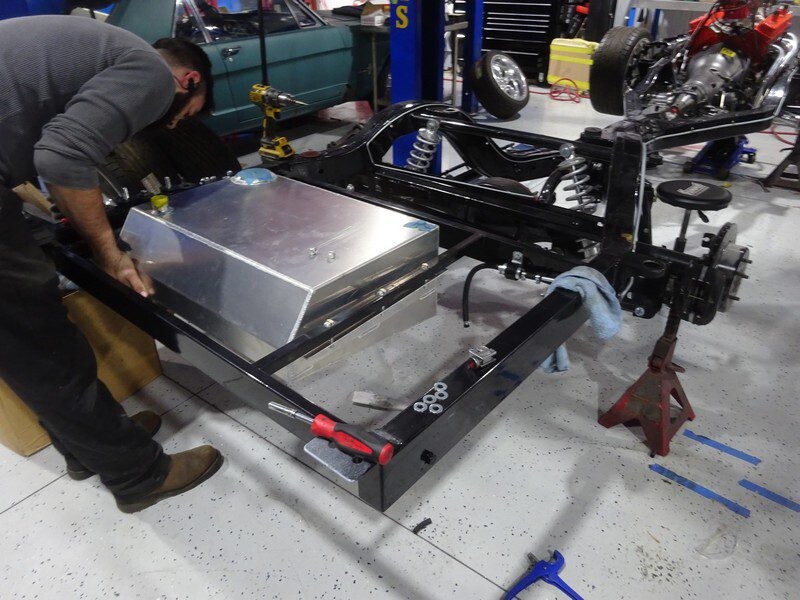 Mechanic installing fuel tank in car frame.