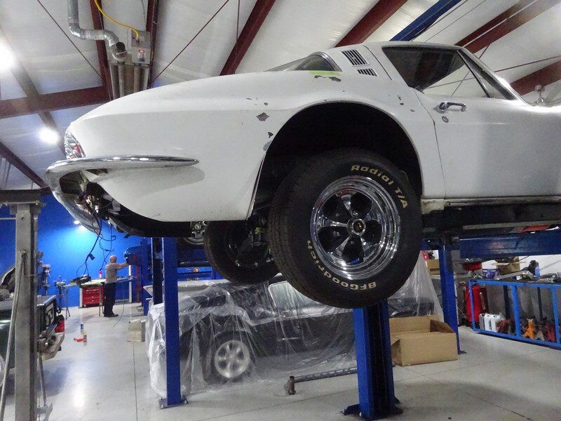 White Corvette on a lift in a garage.