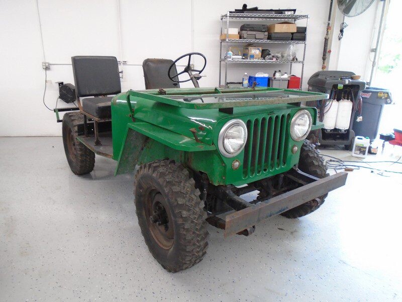 A green jeep standing inside a workshop with white walls